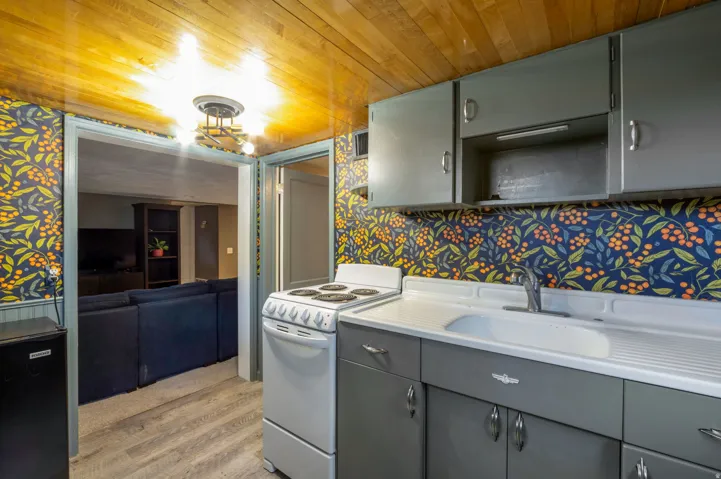Kitchenette featuring grey cabinetry, a white electric range, and a single basin sink with a chrome faucet
