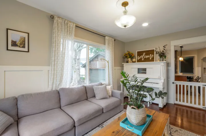 Bright living space featuring warm wood-finish flooring, wainscoting, and large windows with privacy drapes