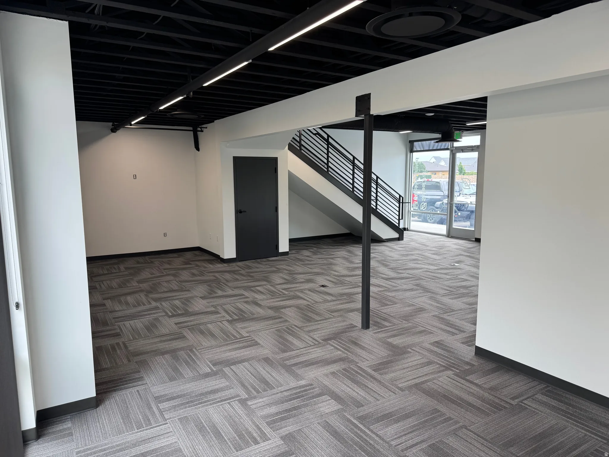 Open-concept space featuring patterned carpet tile flooring, white walls, and a black exposed beam ceiling with track lighting