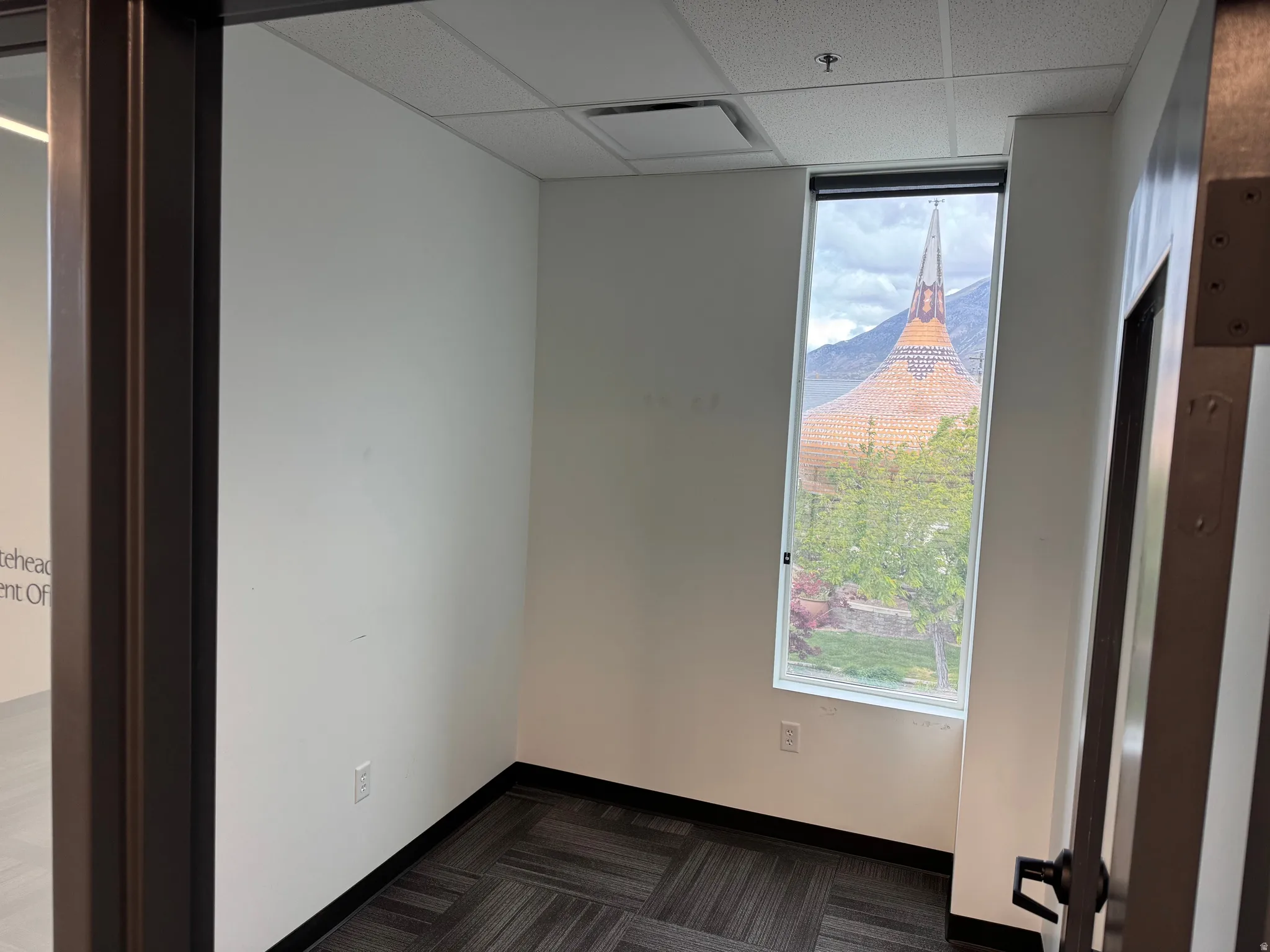 Interior room featuring a tall window with mountain scenery, a unique architectural spire, and mature trees