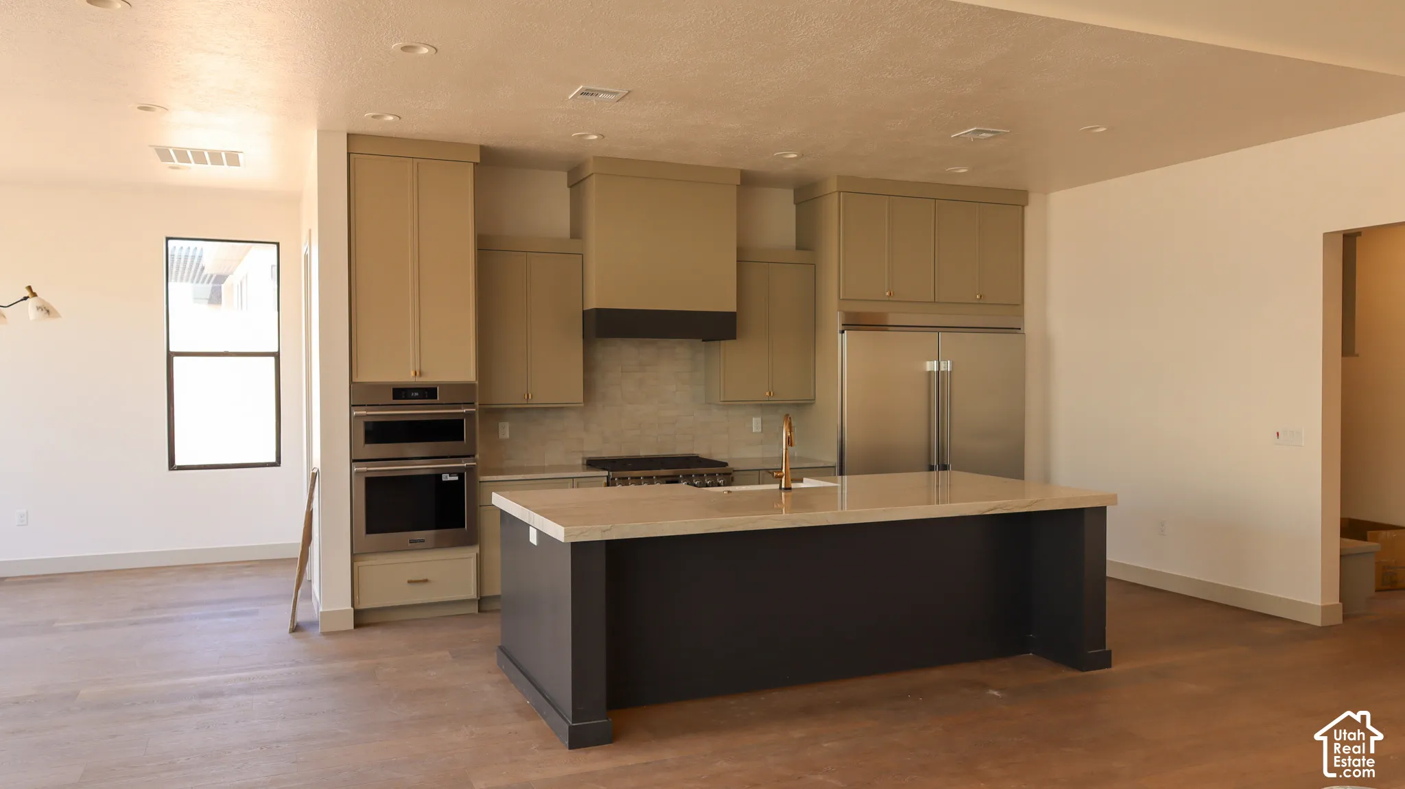 Open-concept kitchen featuring an island with a light-colored countertop, stainless steel appliances, built-in double ovens, and wood-finish flooring