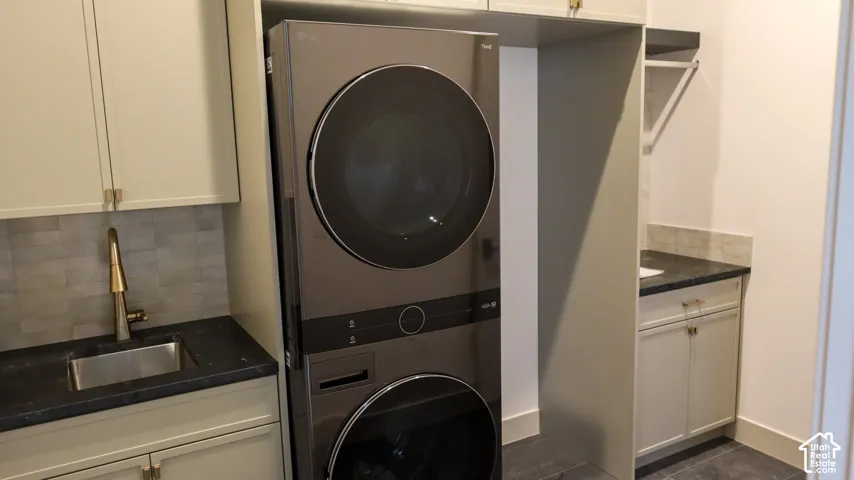 Integrated stacked washer and dryer, under-mount stainless steel sink, dark stone-finish countertop, light neutral cabinetry, and subway tile backsplash