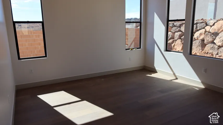 Bright corner room with abundant natural light from multiple windows, dark wood-finish flooring, and clean white walls