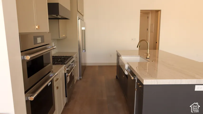 Gourmet kitchen featuring a built-in double oven, gas range, stainless steel appliances, and a central island with an integrated farmhouse sink and brass-finish faucet