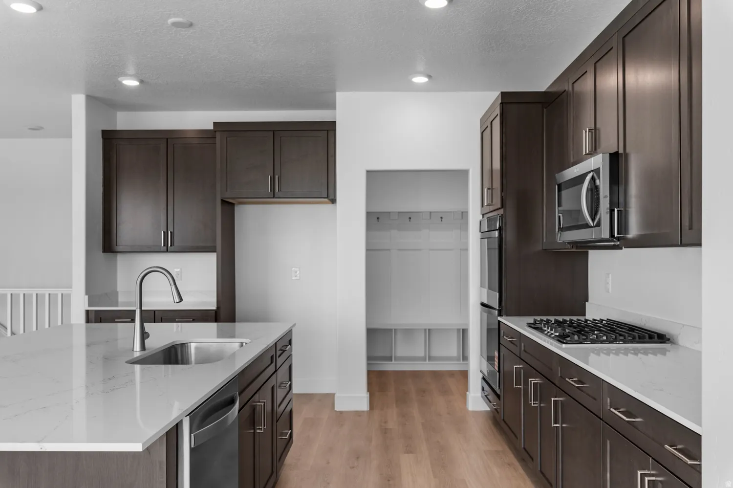 Modern kitchen featuring a spacious island with an undermount sink, dark wood cabinetry, white countertops, stainless steel appliances, and wood-finish flooring