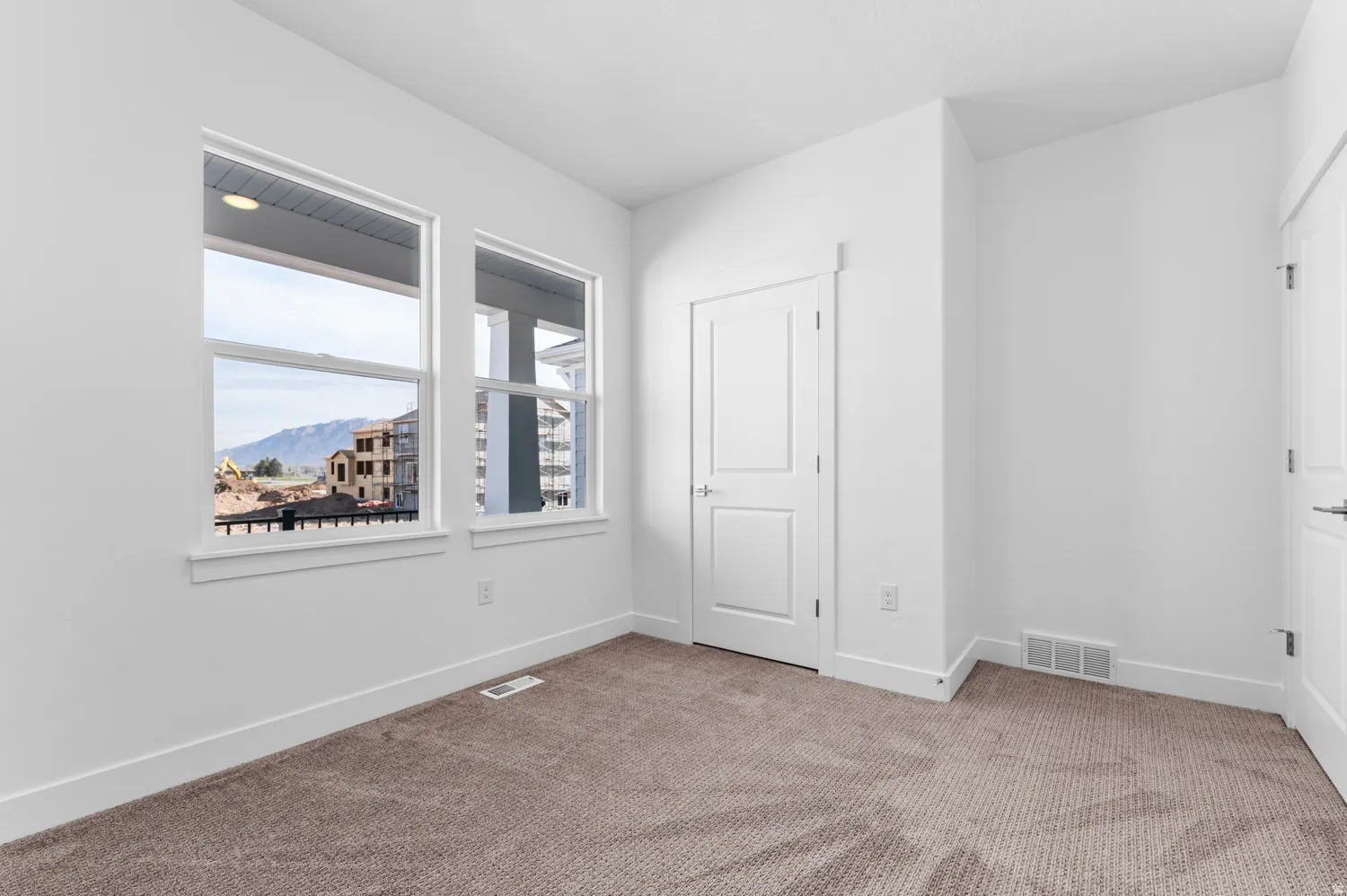 Bright room featuring two large windows, neutral-toned carpeting, white walls, and white trim