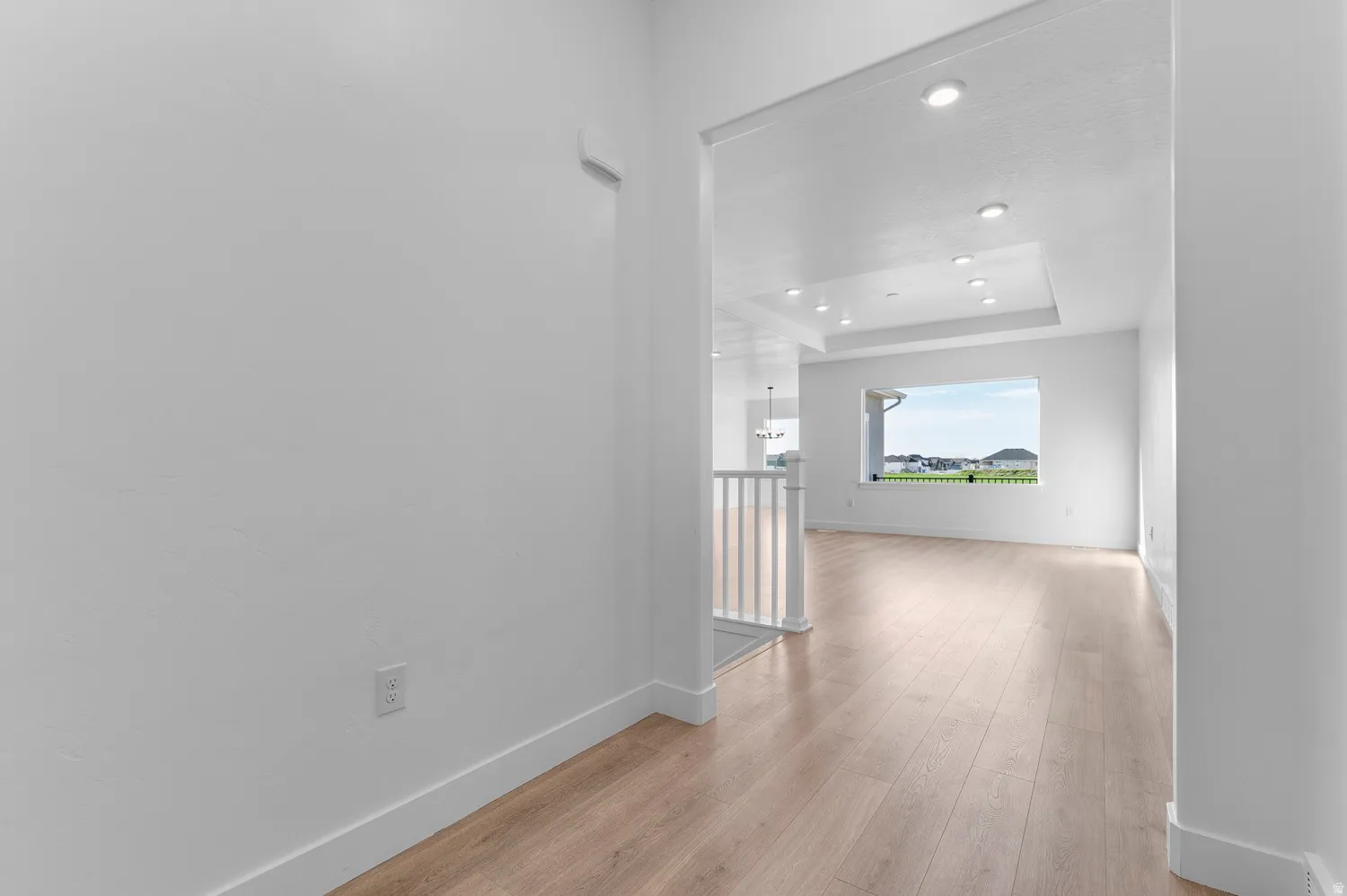 Light wood-finish flooring extending through an open doorway, with a contemporary white railing and a large window