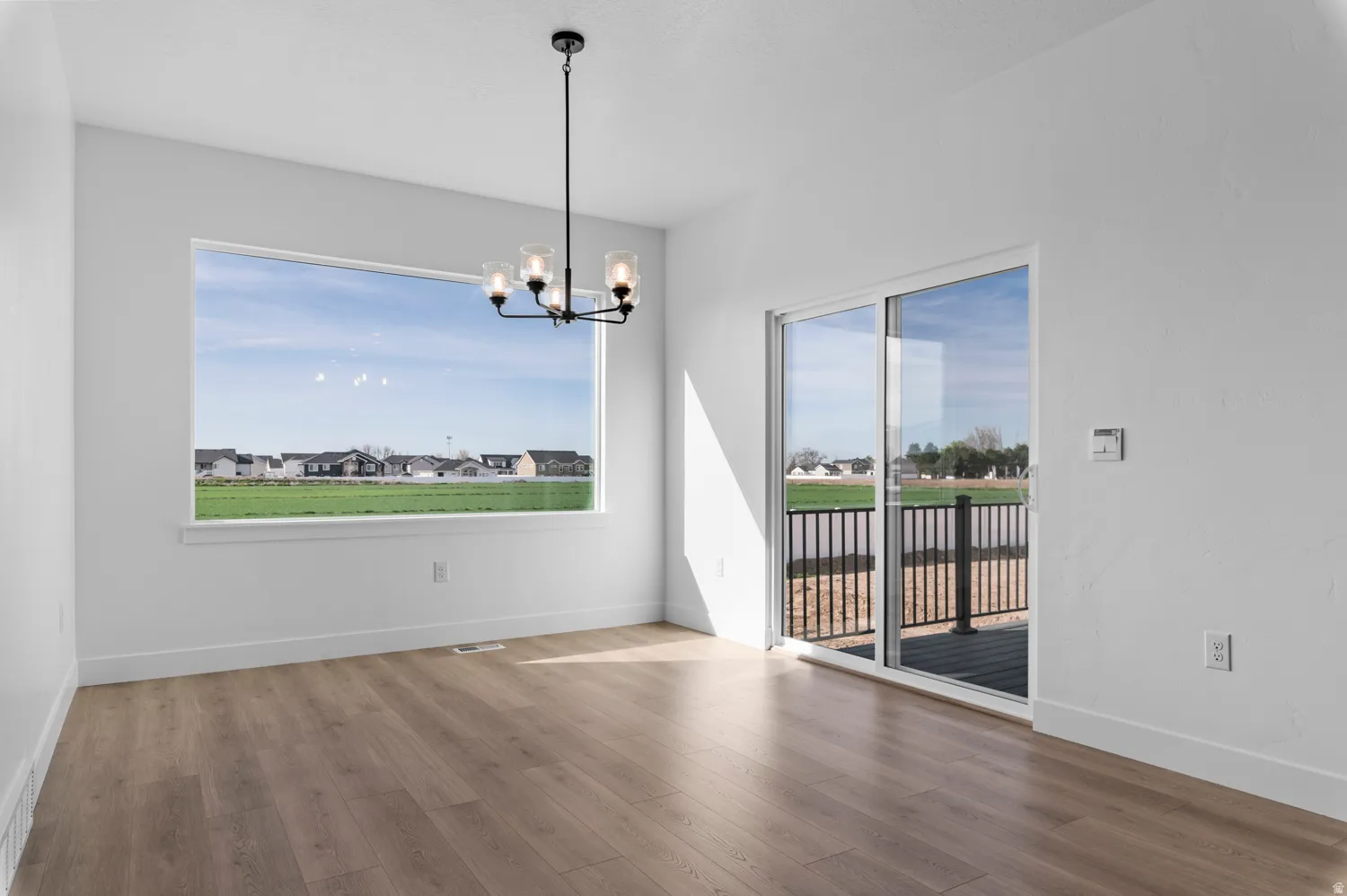 Spacious interior with wood-finish flooring, a contemporary black chandelier, and white baseboards