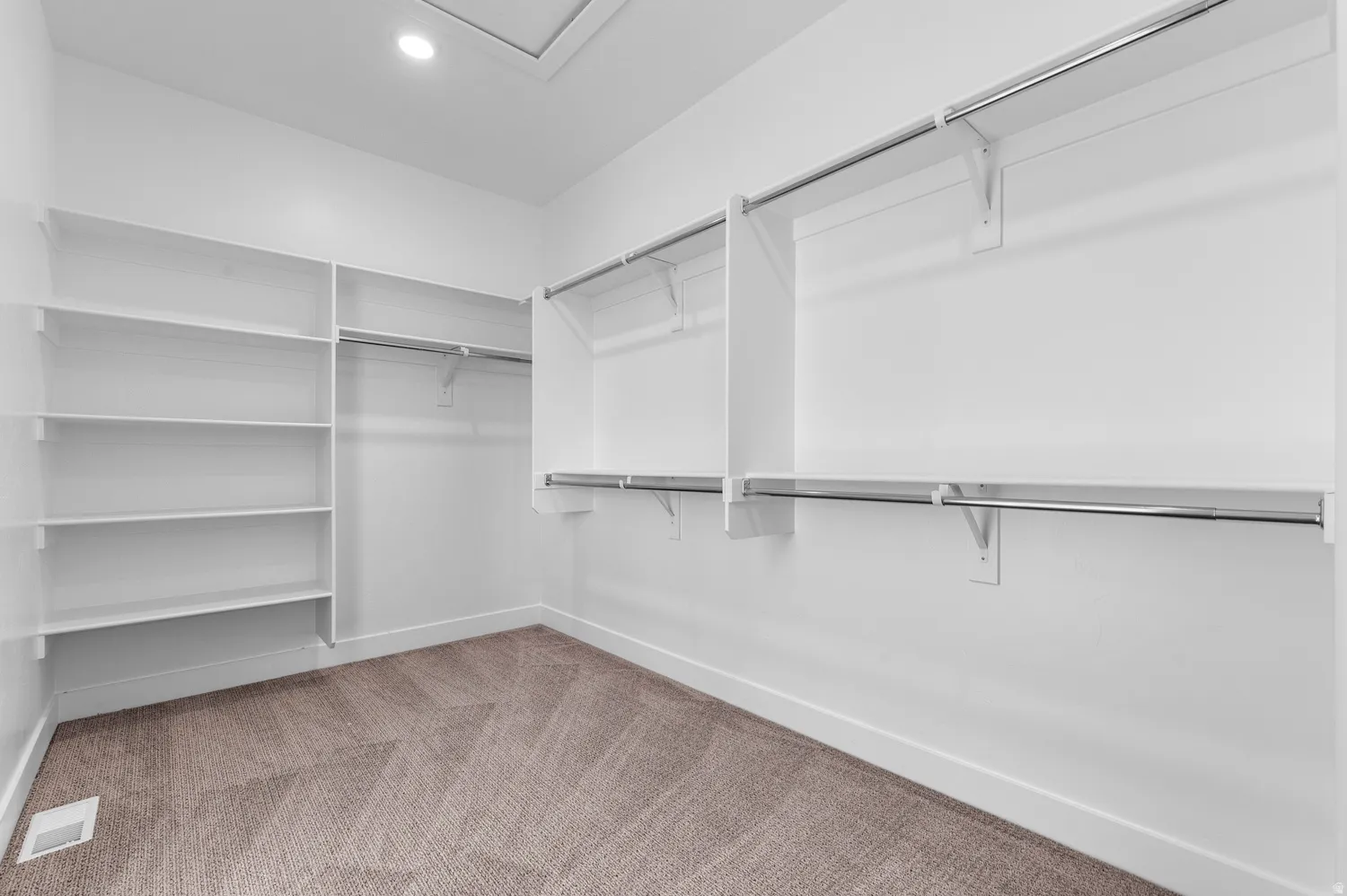 Spacious closet featuring extensive built-in shelving, multiple chrome hanging rods, recessed ceiling lighting, and soft carpet flooring