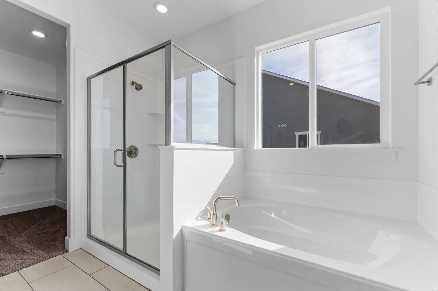 Bright bathroom featuring a glass-enclosed shower with brushed nickel hardware, a white built-in bathtub, and a large window