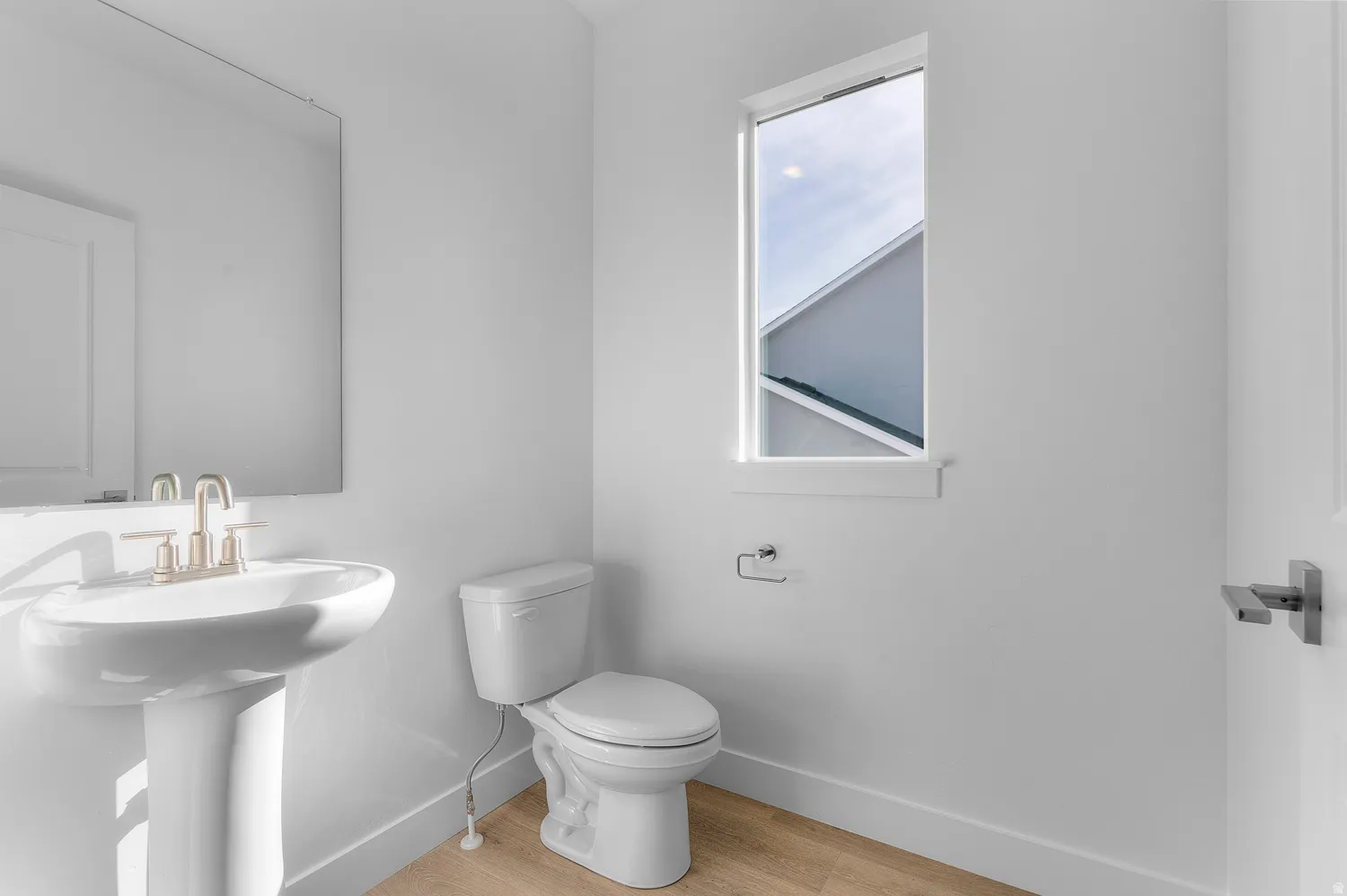 Pedestal sink with brushed nickel faucet, full vanity mirror, and wood-finish flooring