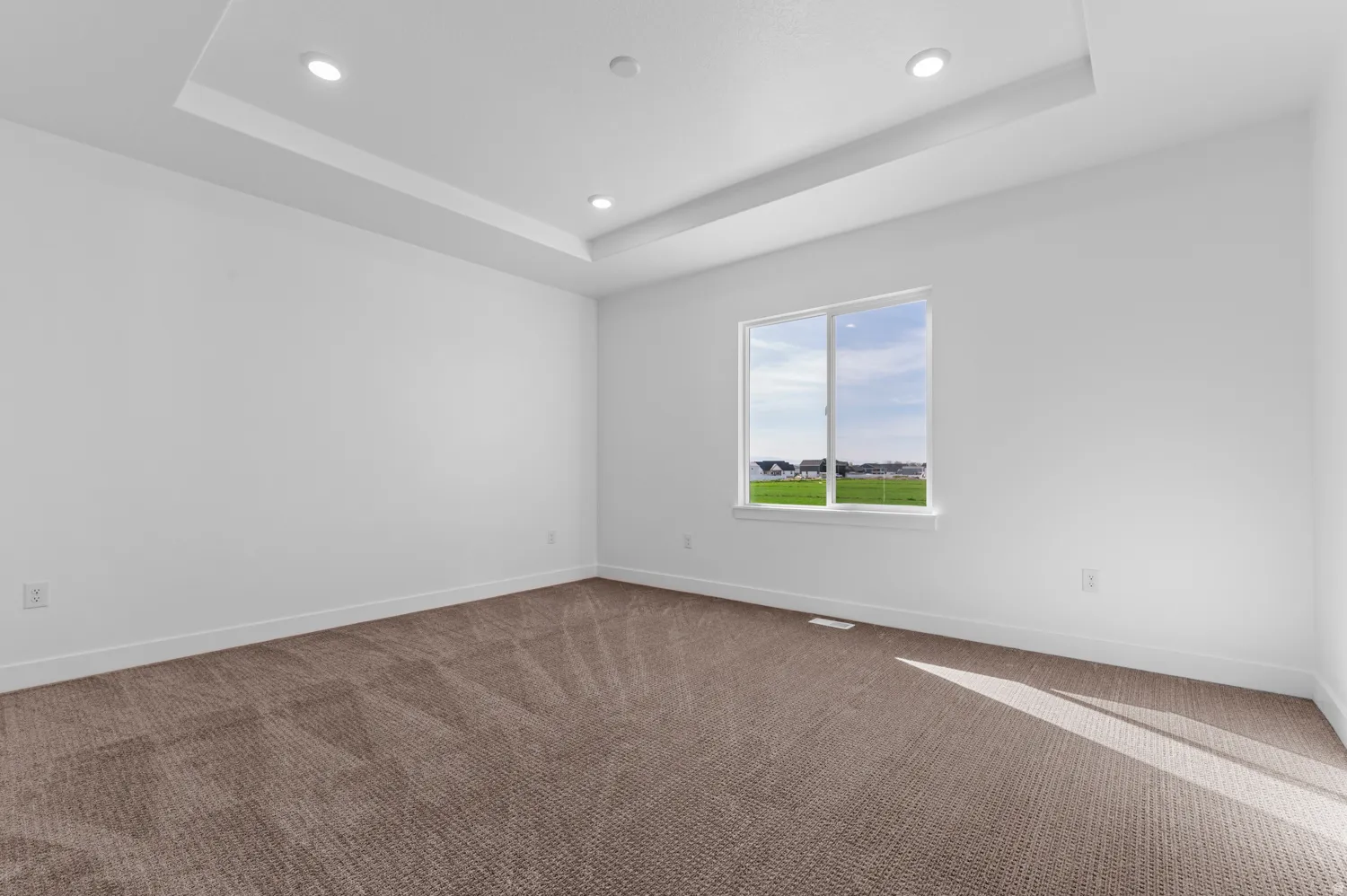 Spacious room featuring a tray ceiling with recessed lighting, a large window, white baseboards, and neutral-toned carpeting