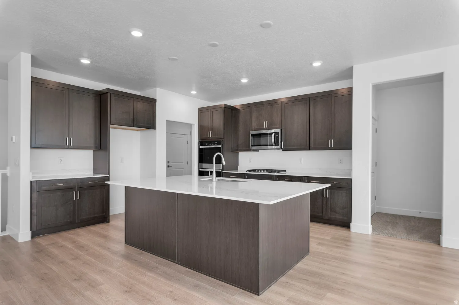 Modern kitchen featuring dark wood-finish cabinetry, white countertops, and stainless steel appliances