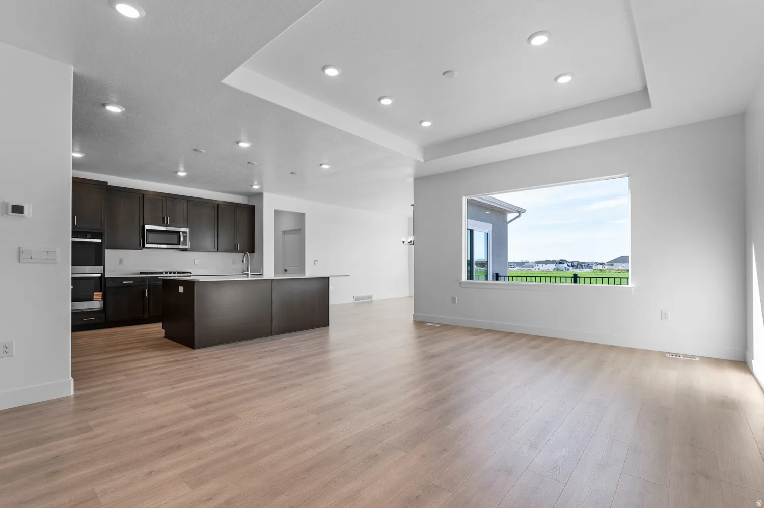 Open-concept living area featuring light wood-finish flooring and a recessed tray ceiling with integrated lighting