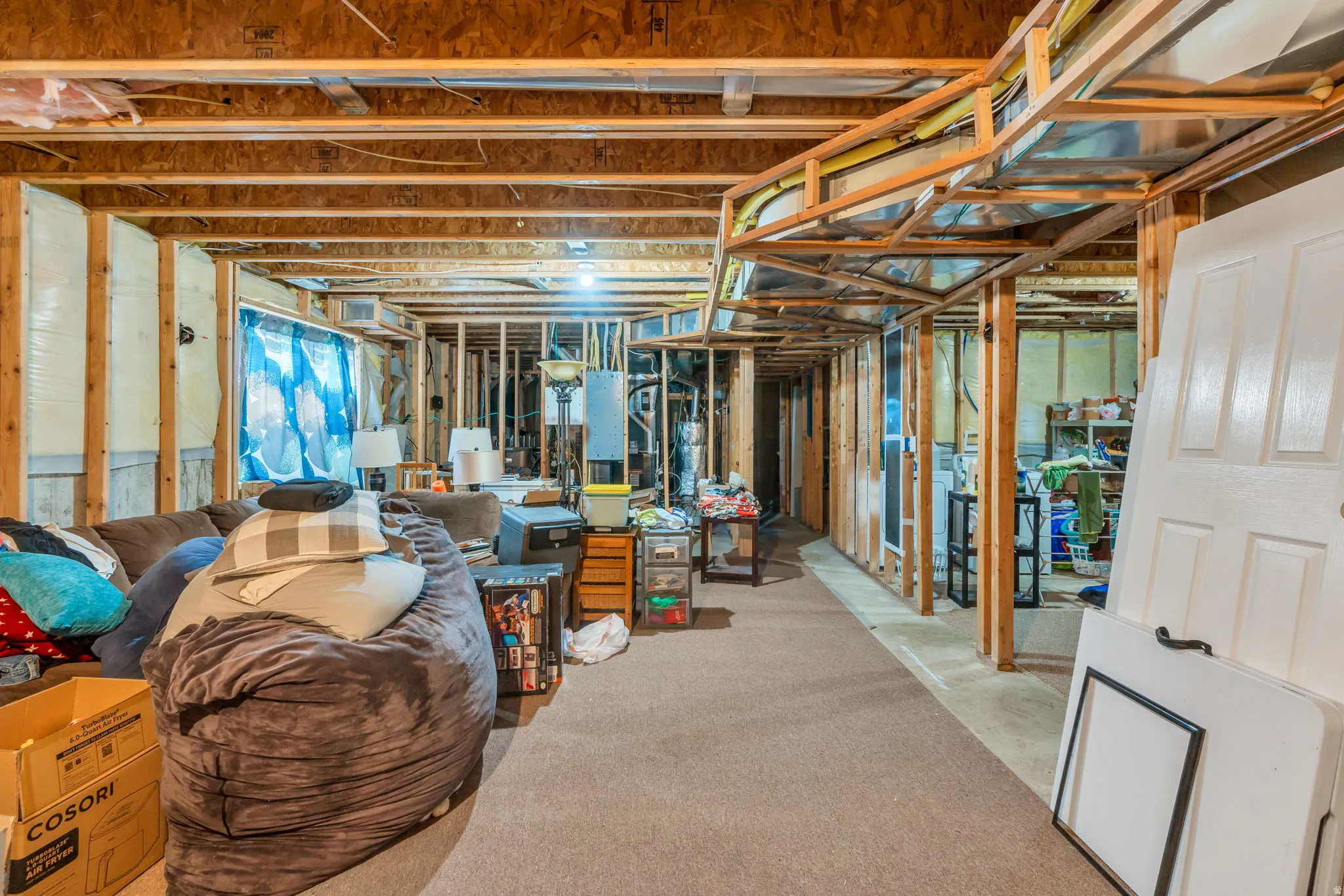 Unfinished basement featuring exposed wood framing, an open ceiling with visible joists, and existing carpeted flooring