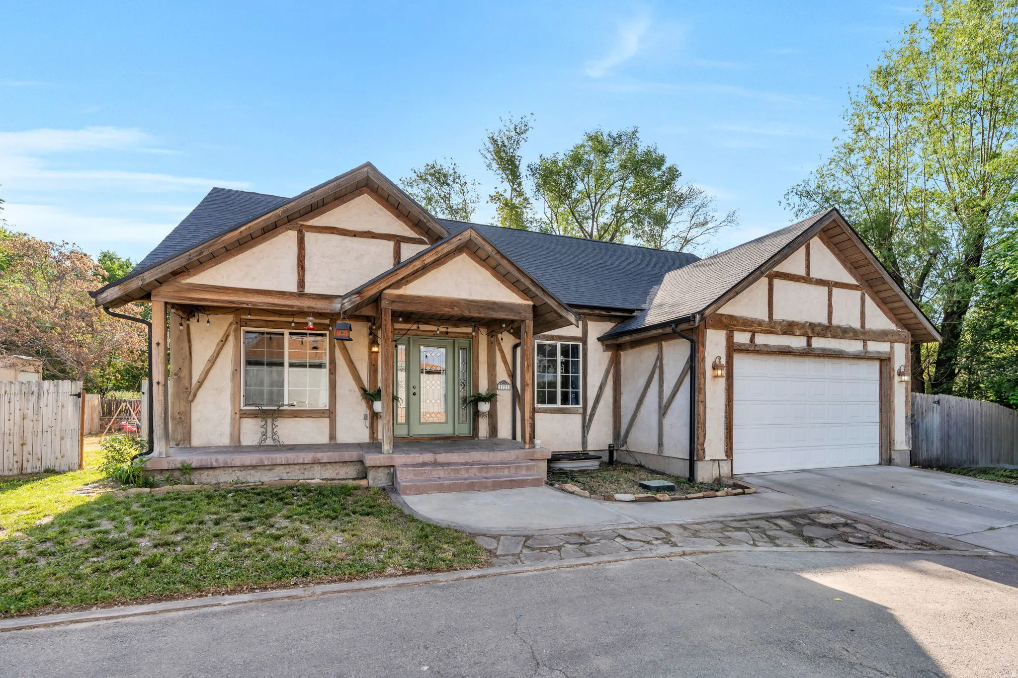 Tudor-style exterior featuring a prominent two-car garage, dark shingle roof, and a covered porch entry with exposed wood beams