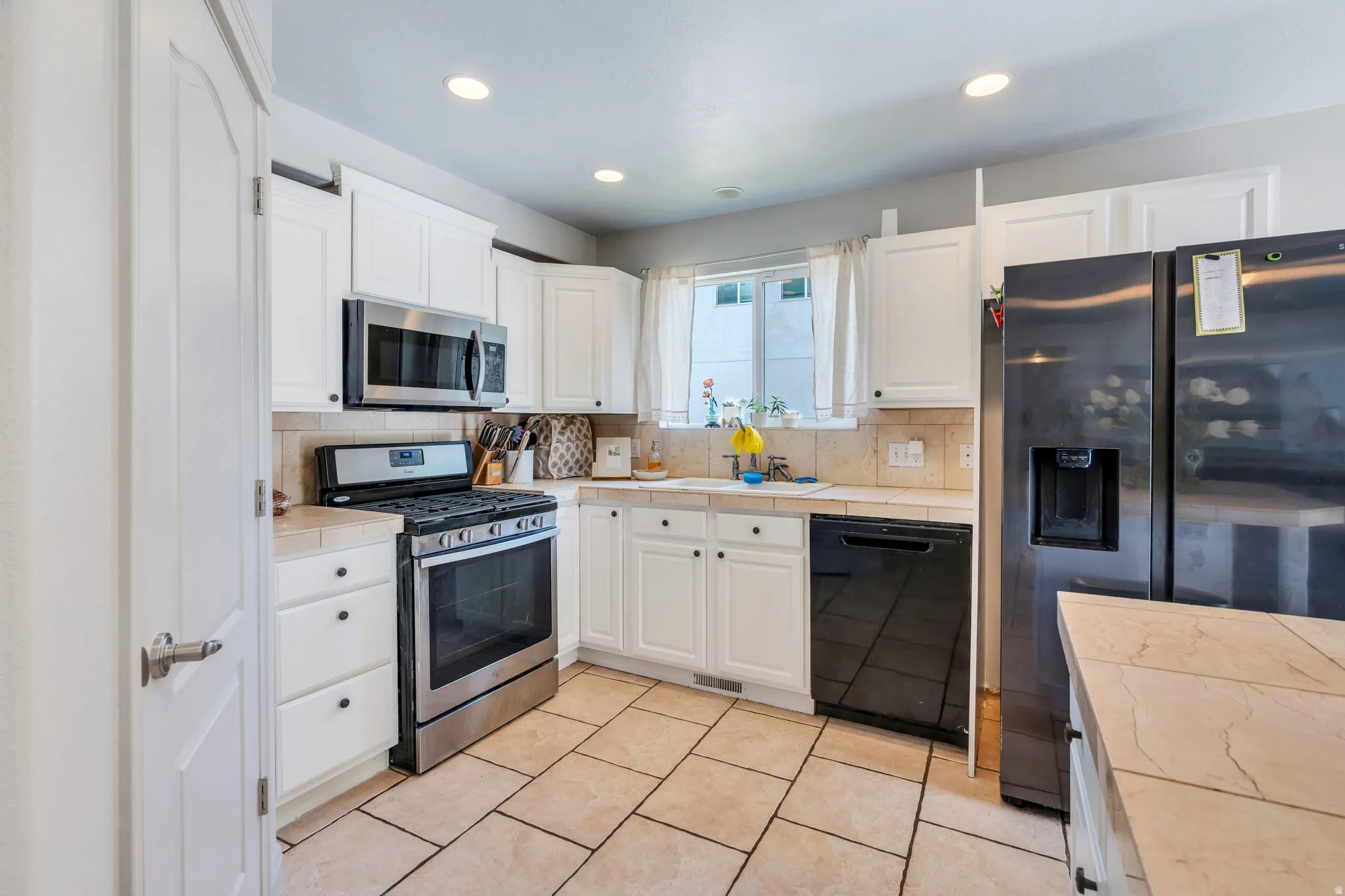 Kitchen featuring white cabinetry with black hardware, stainless steel appliances, beige tile flooring, and light-toned countertops