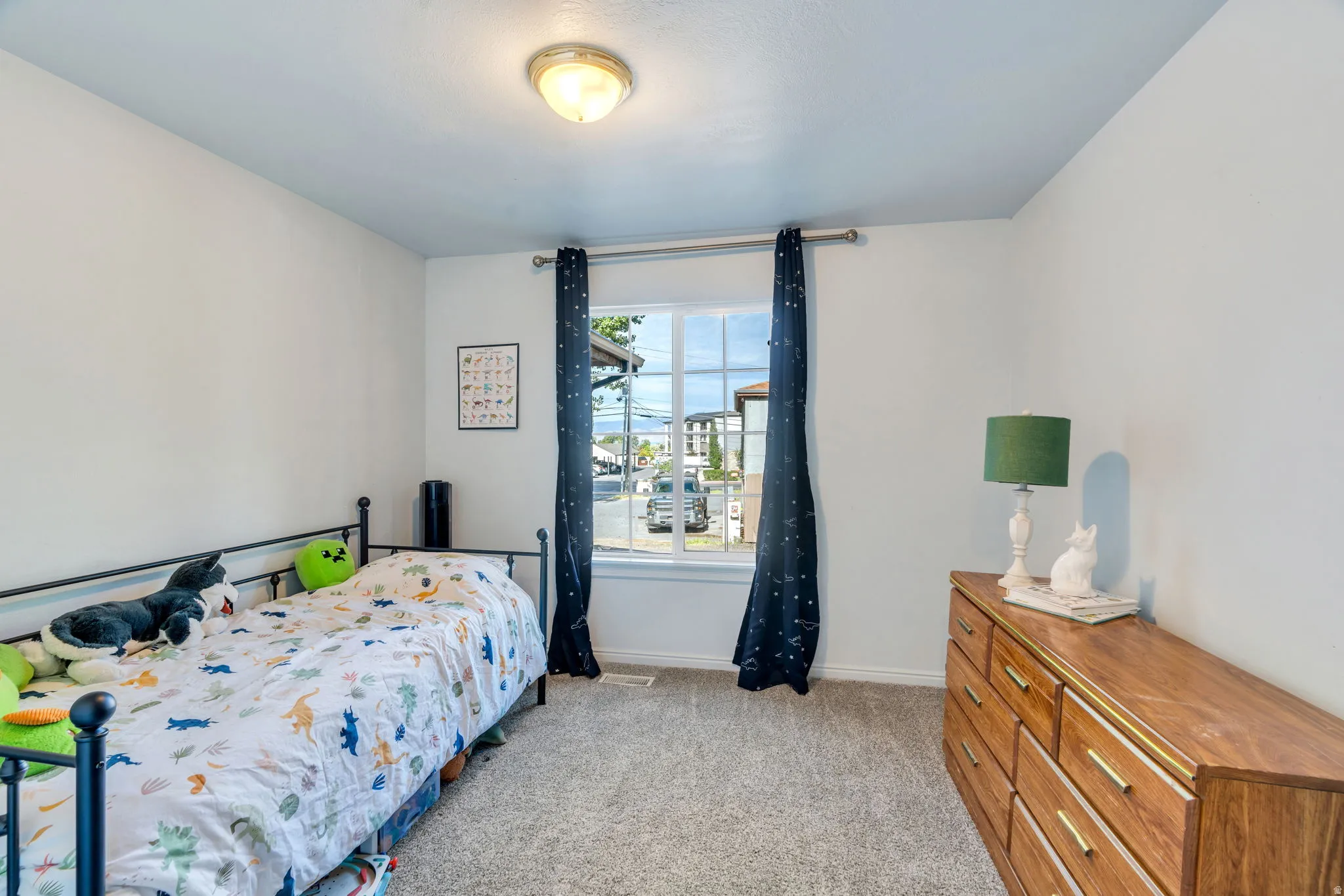 Neutral wall paint, plush carpet flooring, and a single window with dark curtains define this bright room