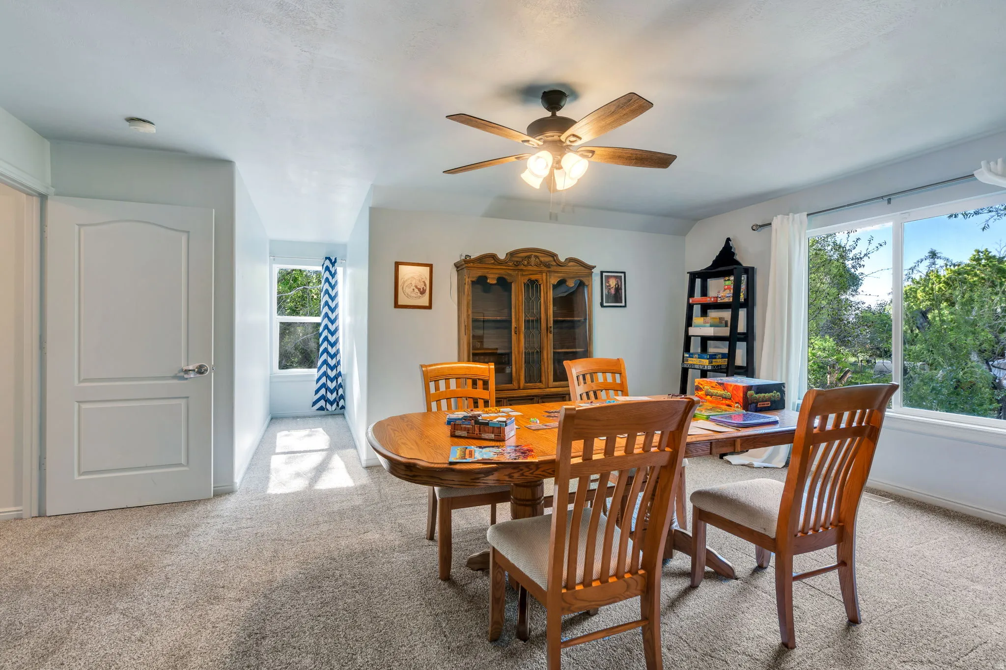 Carpeted room featuring a ceiling fan with integrated lighting, multiple windows, and a built-in recessed window nook