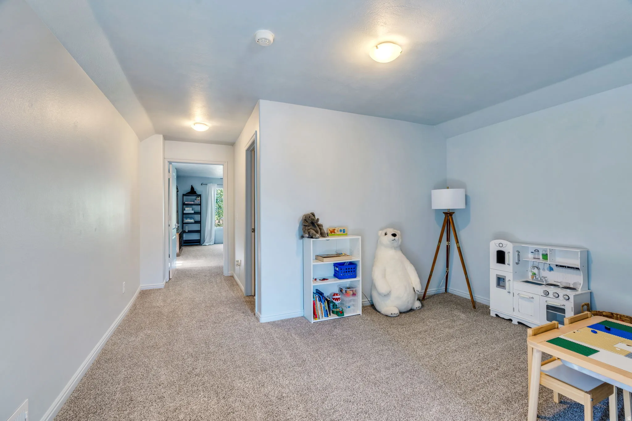 Carpeted room with light-toned walls and ceiling, featuring recessed lighting and a doorway opening to a hallway