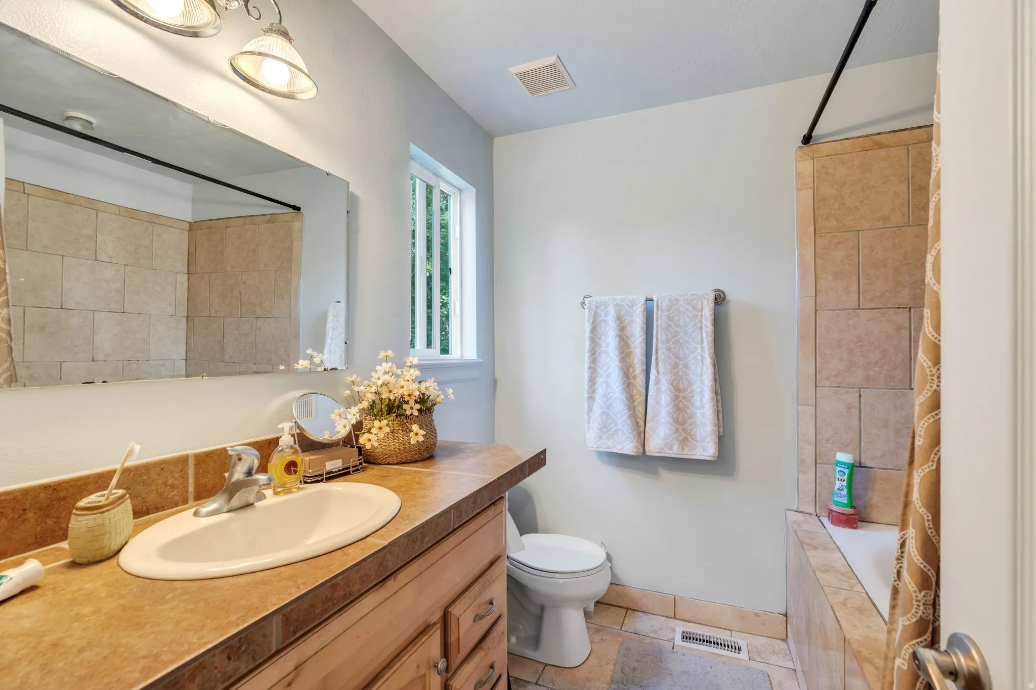 Bathroom featuring a wood-finish vanity with an oval undermount sink, a tiled countertop, and a large wall-mounted mirror