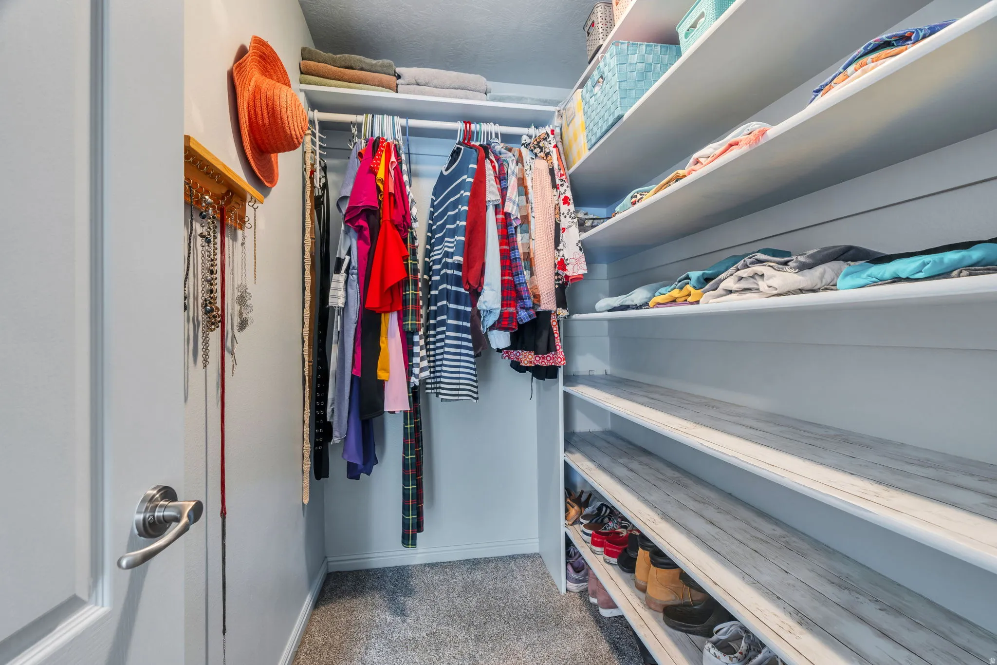 Walk-in closet featuring built-in shelving, hanging rods, carpet flooring, and a door with brushed nickel hardware