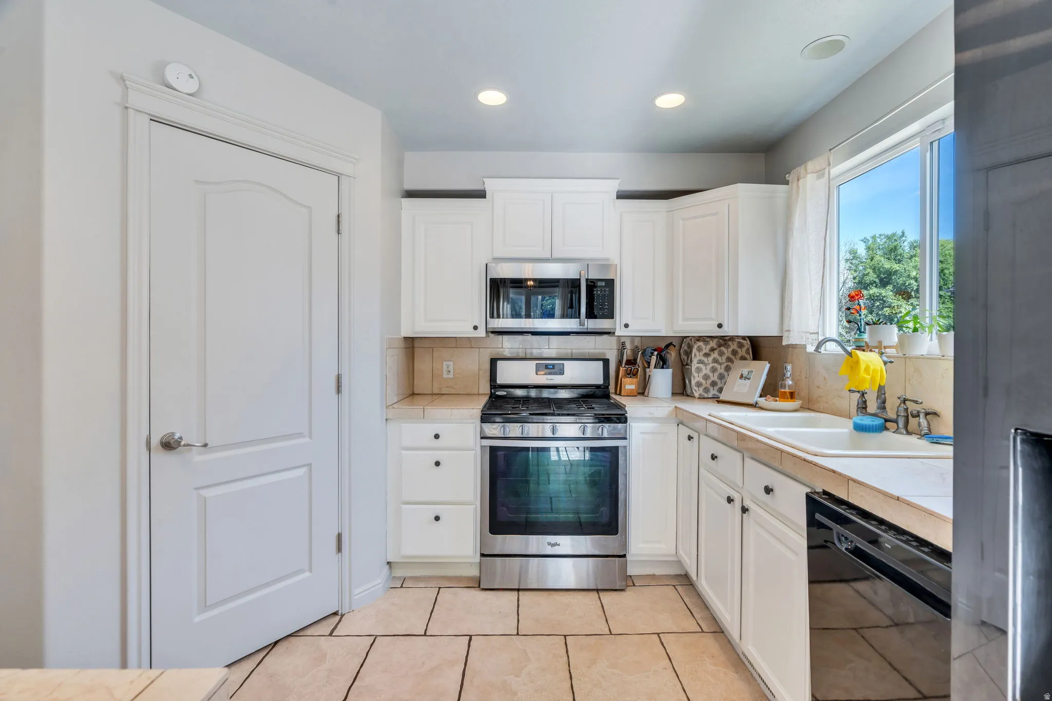 Kitchen featuring white cabinetry, stainless steel range and microwave, tile flooring, and a window above the sink