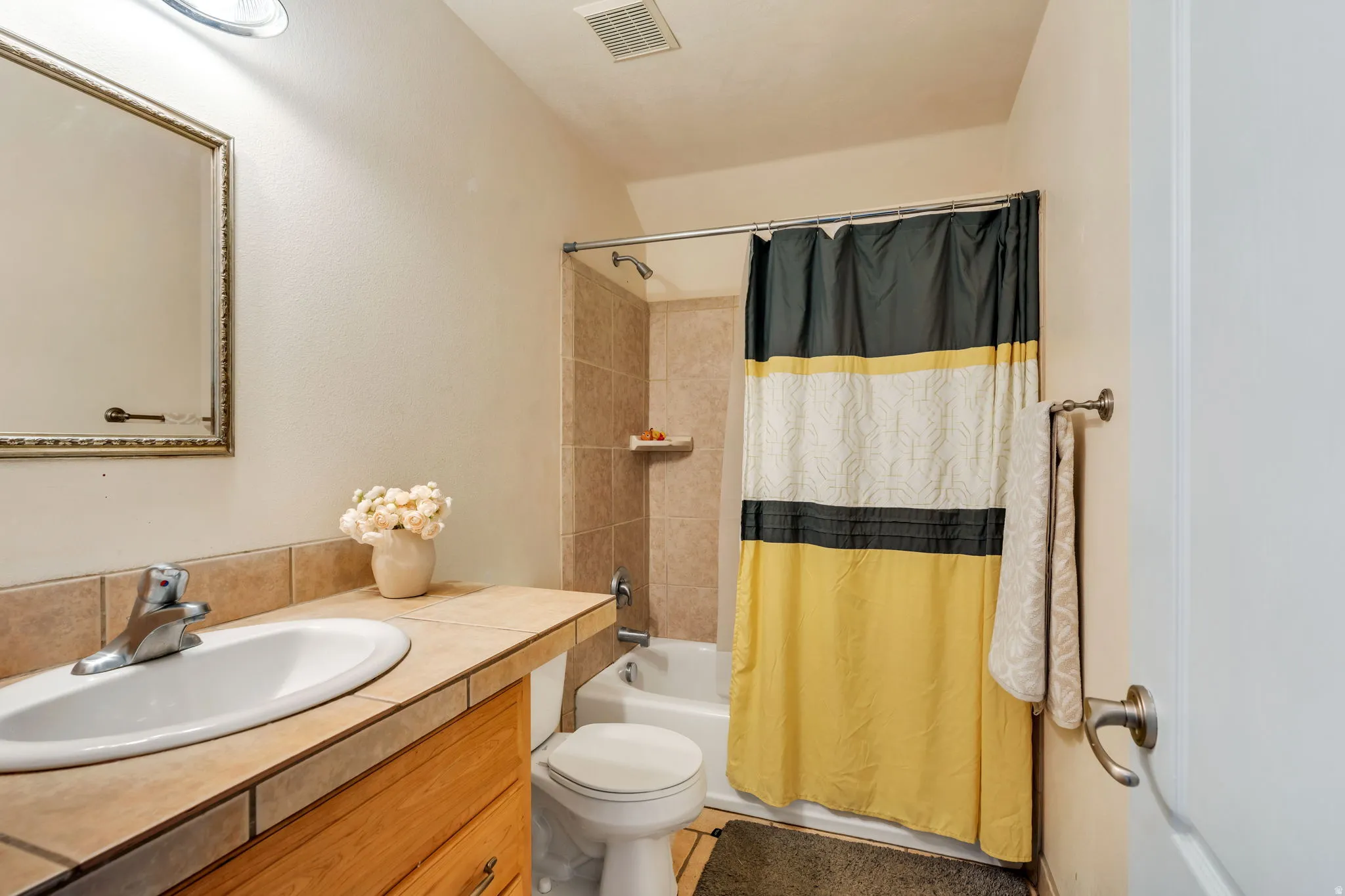 Bathroom featuring a built-in vanity with a tiled countertop, undermount sink, and wood-finish cabinetry