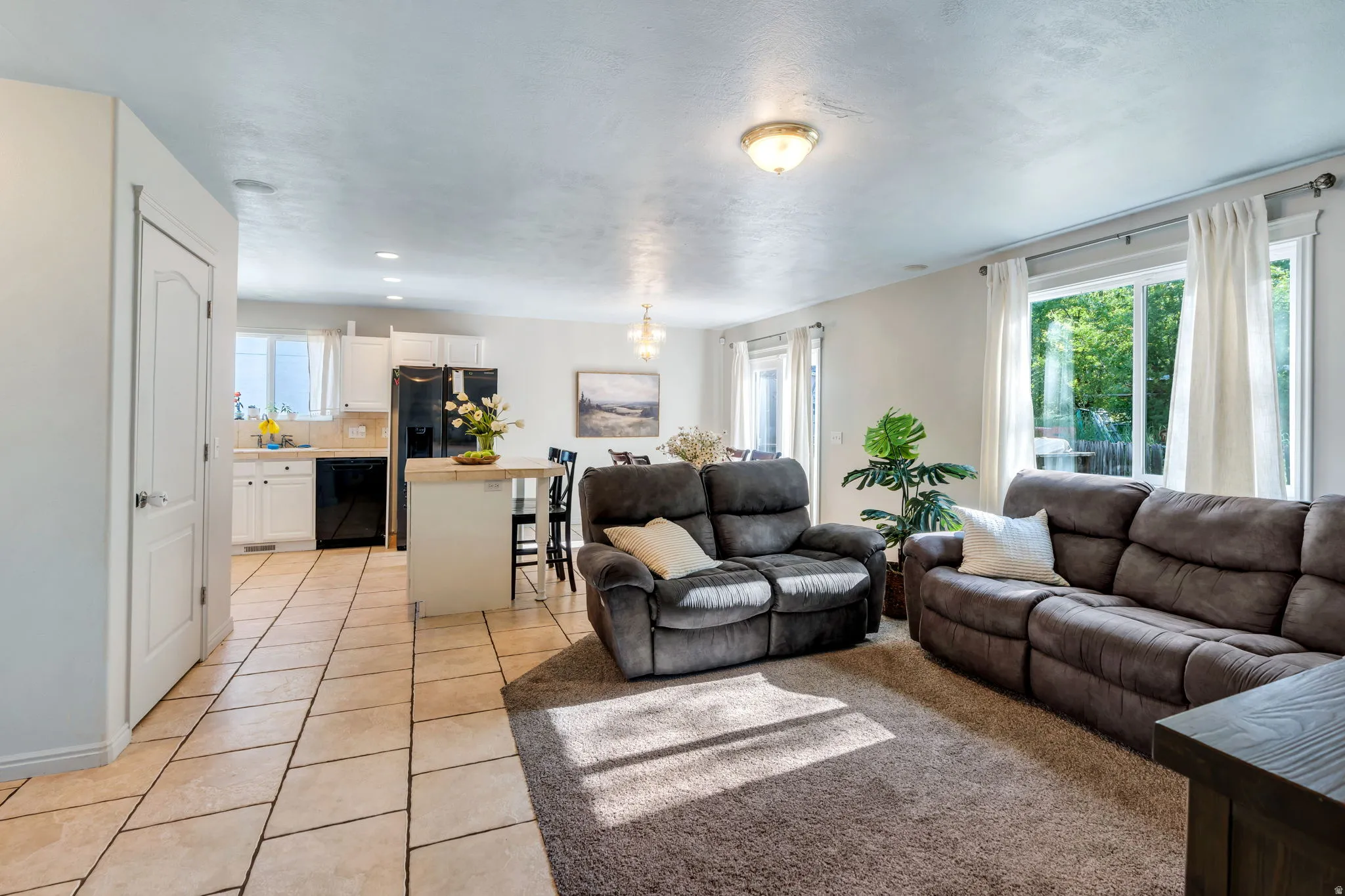 Open-concept living space featuring a carpeted lounge area, a kitchen with white cabinetry and black appliances, a central island, and tile flooring
