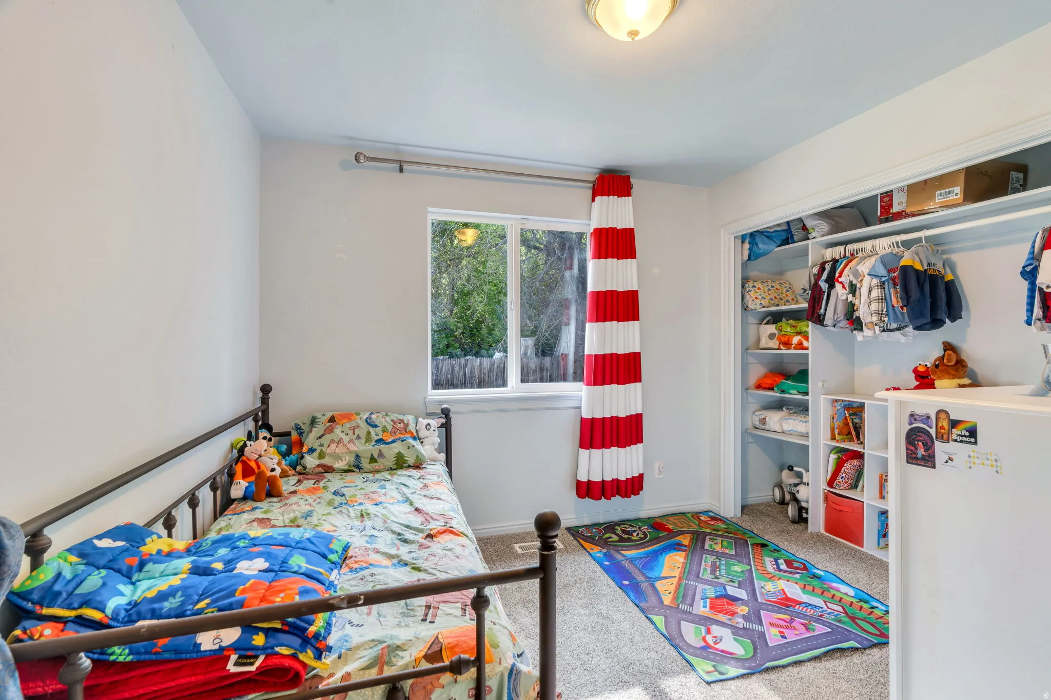 Carpeted room featuring a window with white trim, a built-in closet with shelving and hanging rods, and a flush-mount ceiling light fixture