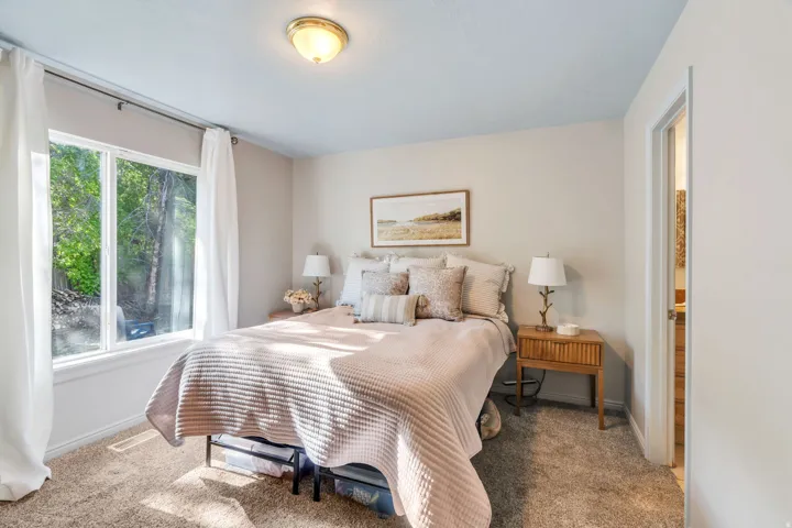 Bedroom featuring neutral-toned walls, plush carpeting, and a window with white trim