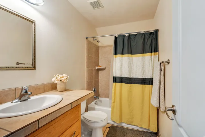 Bathroom featuring a built-in vanity with a tiled countertop, undermount sink, and wood-finish cabinetry