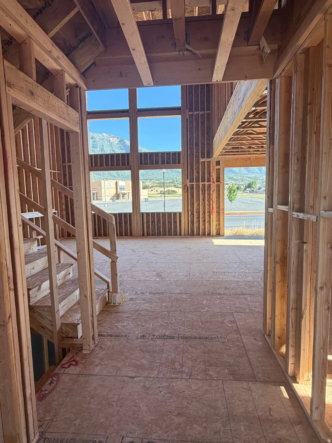 Framed interior space featuring a multi-story window wall, mountain scenery, exposed ceiling joists, and an unfinished staircase