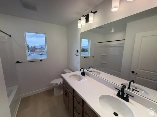 Dual-sink vanity with a quartz countertop, matte black fixtures, full-width vanity mirror, and wood-finish flooring