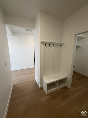 Built-in white mudroom bench featuring integrated storage cubbies, paneled wall detail, and overhead coat hooks, set against wood-finish flooring