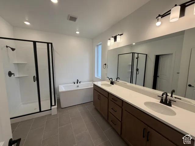 Owner's bathroom. Dual-sink vanity with light-toned solid surface countertops, wood-finish cabinetry, frameless glass shower enclosure with matte black fixtures, and a freestanding soaking tub