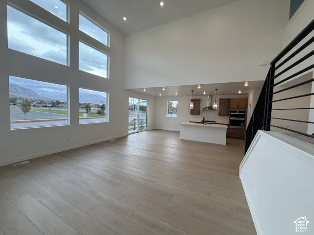 Double-height ceiling with floor-to-ceiling windows, wood-finish flooring, kitchen island with built-in cabinetry, recessed lighting, and metal stair railing