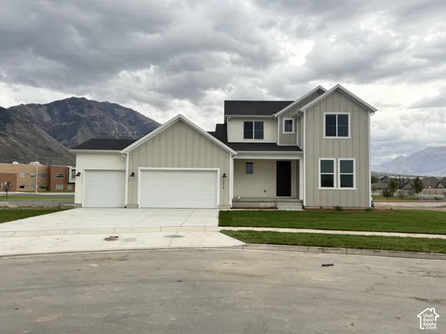 Two-story exterior with vertical siding, three-car garage, covered entryway, and mountain backdrop