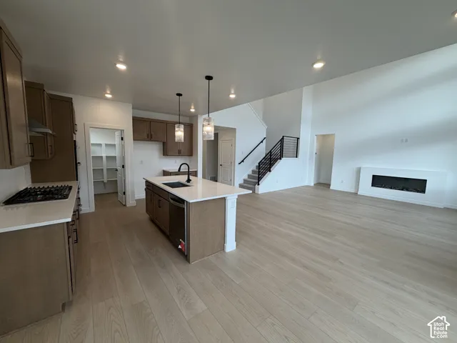 Kitchen featuring wood cabinetry, a quartz-topped island with an under-mount sink, integrated gas range, recessed lighting, and an in-wall fireplace with wood-finish flooring throughout