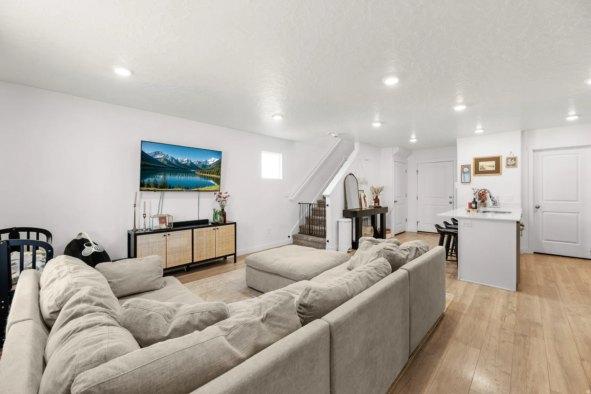Open-concept living area with wood-finish flooring, recessed lighting, white walls, a staircase with dark wood-finish treads, and a kitchen island with a light-toned countertop