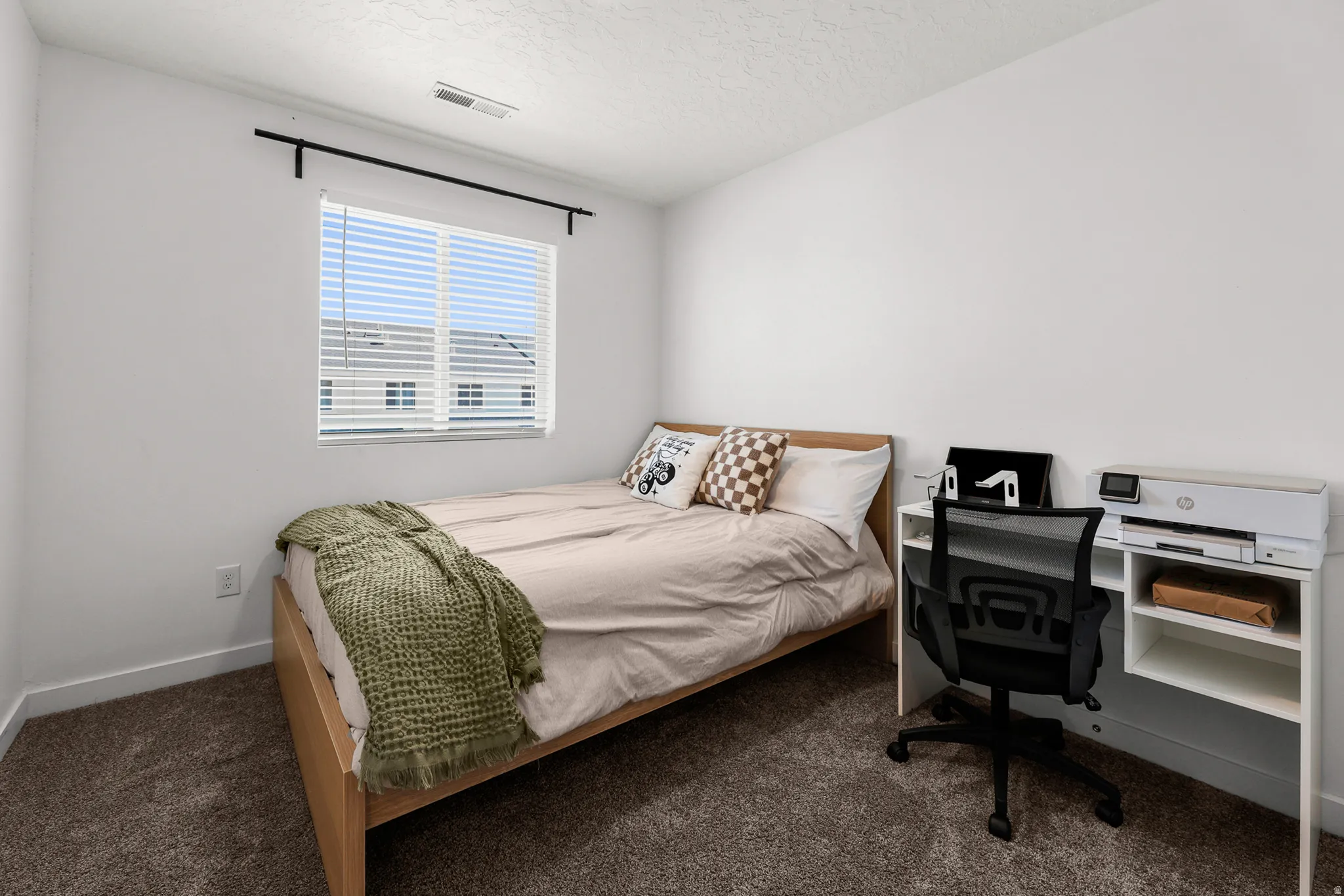 Carpeted room featuring a window with blinds, white walls, and a built-in shelf unit