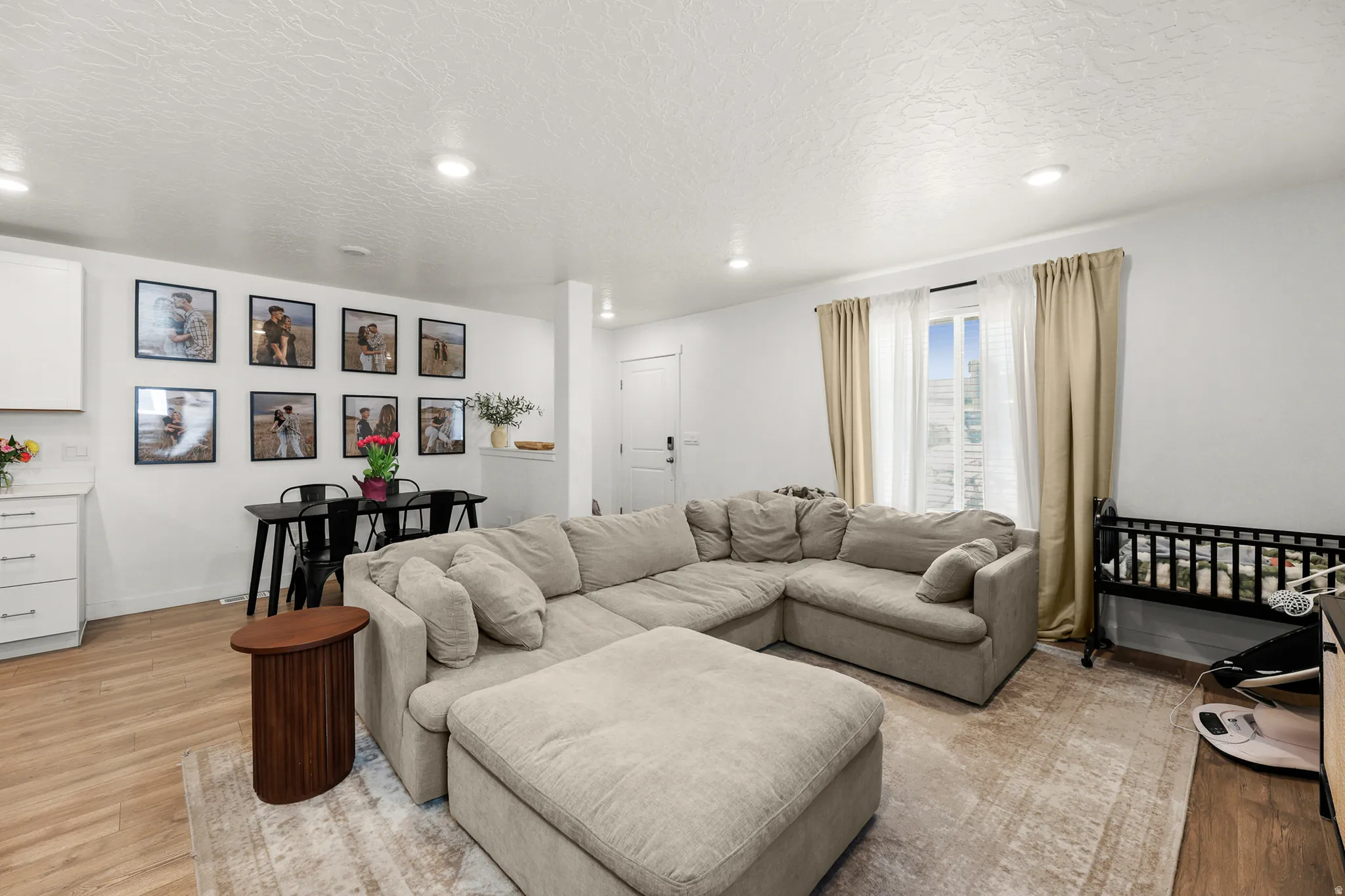 Open-concept living space featuring wood-finish flooring, recessed lighting, and a prominent window with vertical blinds and drapes