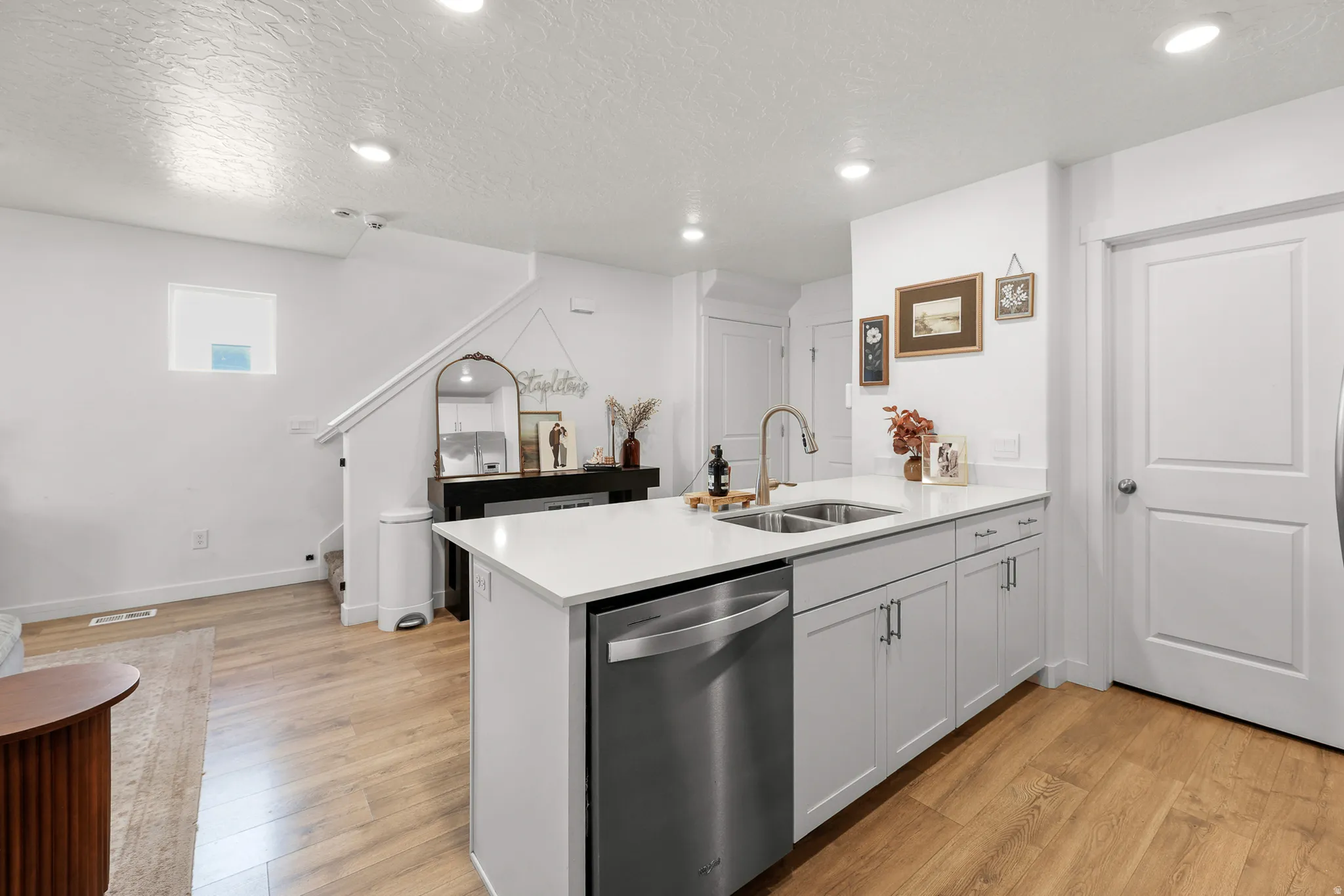 Kitchen island featuring a stainless steel dishwasher, double basin sink with a gooseneck faucet, light-toned cabinetry, and a white countertop