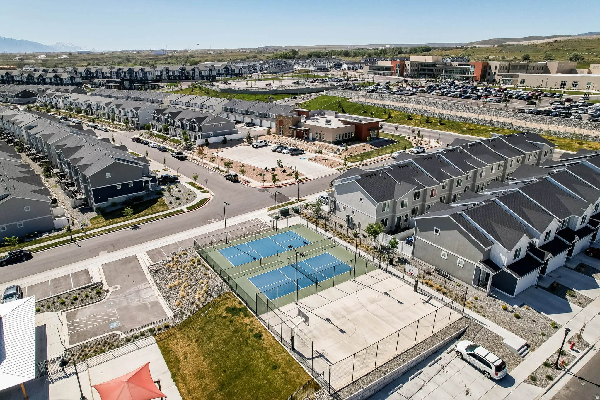 Aerial perspective showcasing a community with rows of townhomes, a basketball court, and two tennis courts