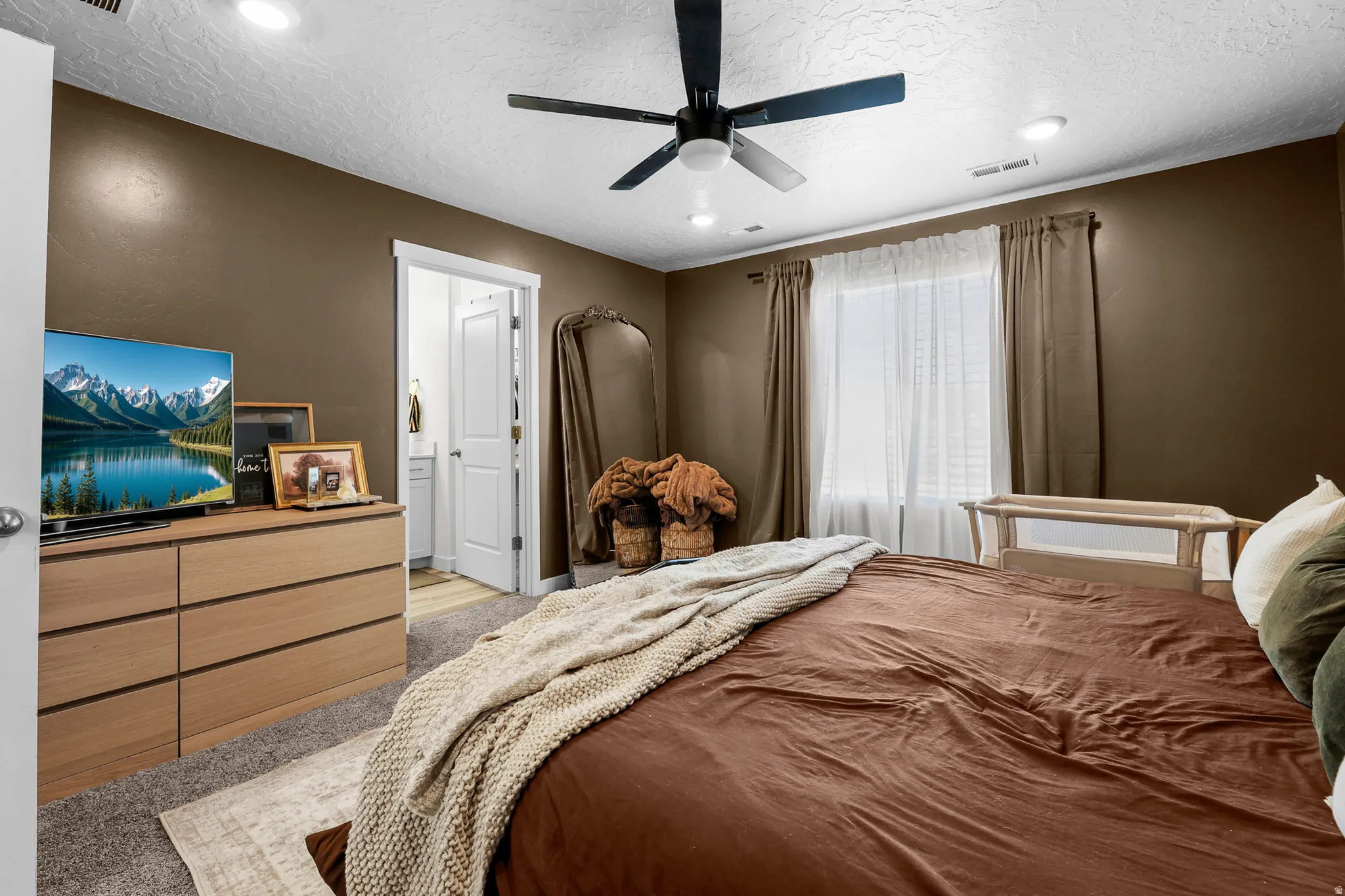 Carpeted room featuring a ceiling fan with integrated lighting, recessed ceiling lights, a large window with blinds and drapes, and a white door leading to a separate area