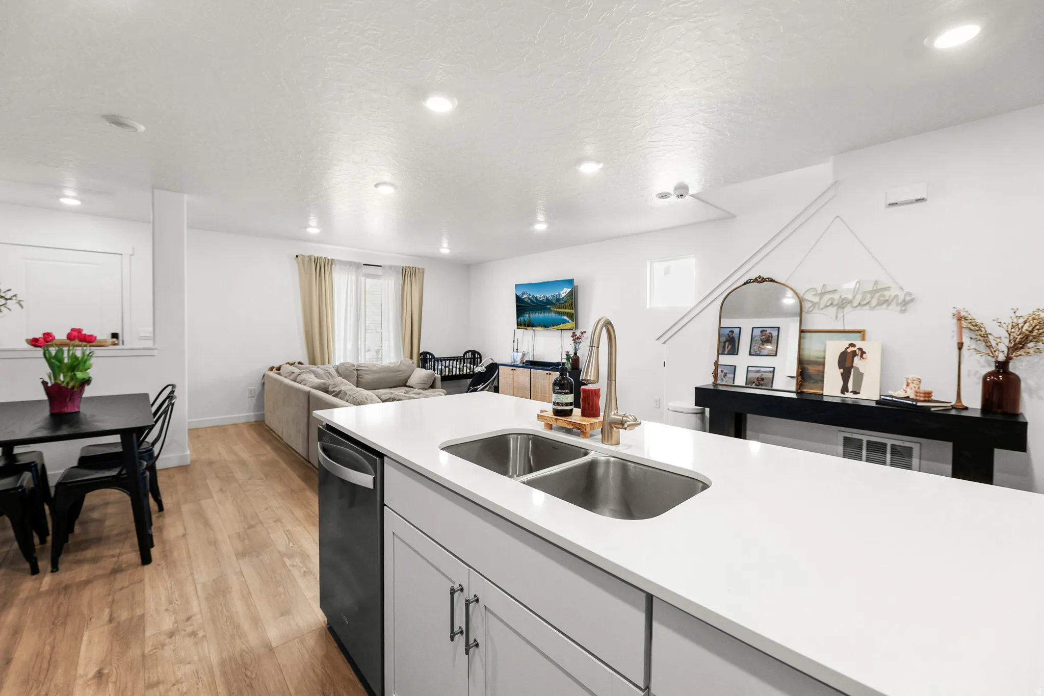 Kitchen island with white countertops and an undermount double basin sink, featuring a stainless steel faucet, dishwasher, and light gray cabinetry