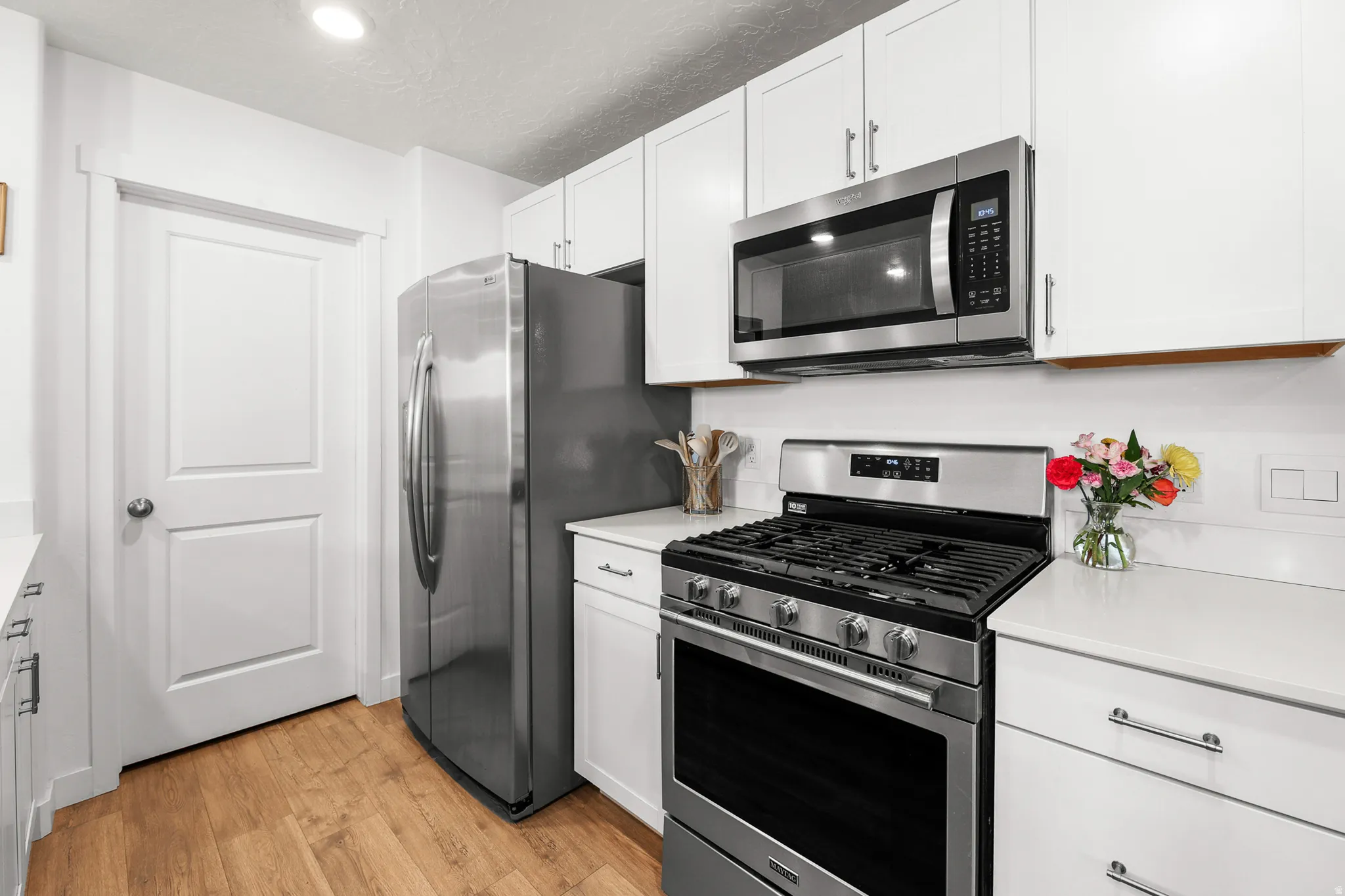 Kitchen featuring white cabinetry, stainless steel appliances, white countertops, and wood-finish flooring