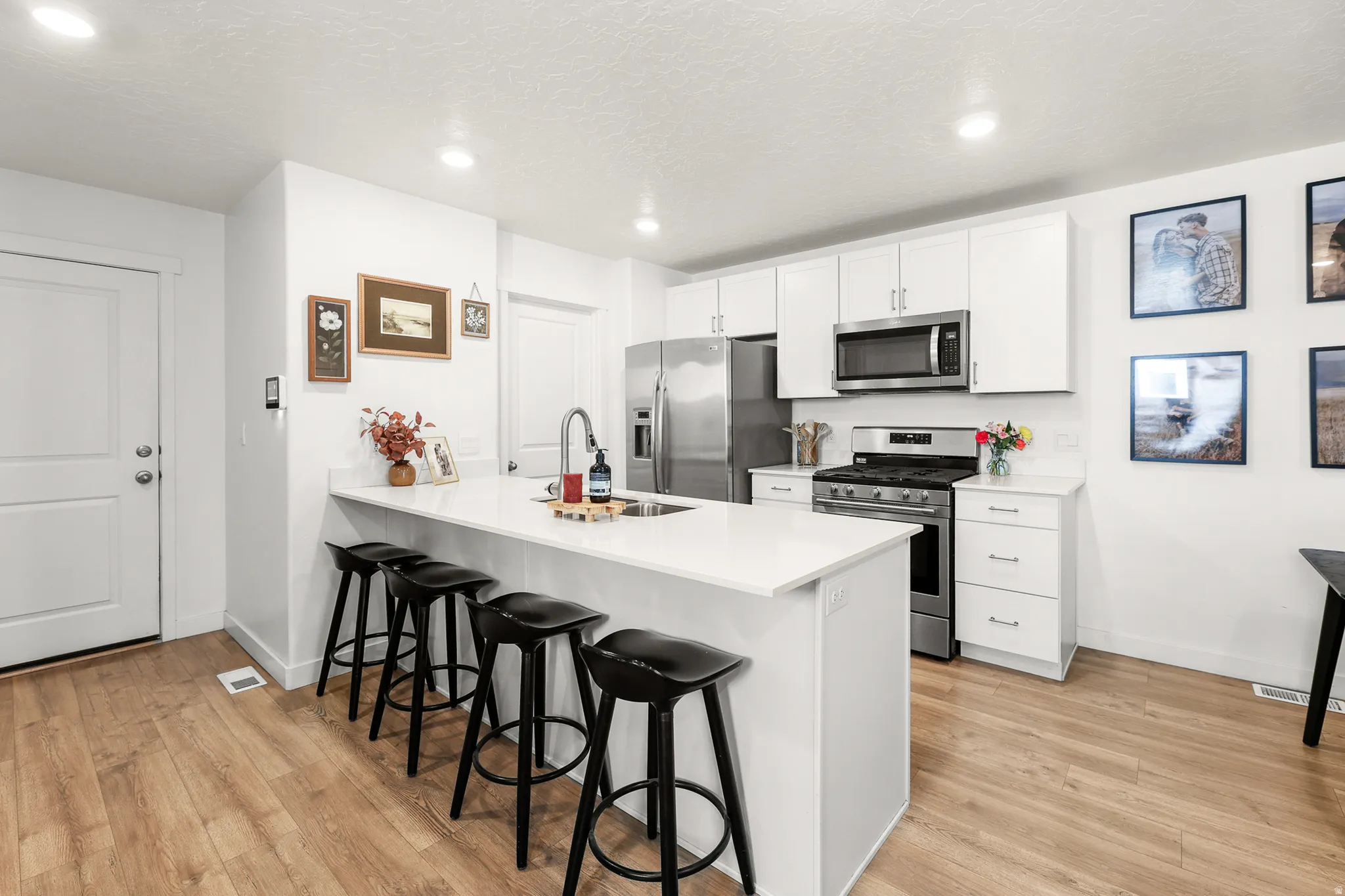 Contemporary kitchen featuring white cabinetry, stainless steel appliances, a spacious island with an integrated sink, white countertops, and wood-finish flooring