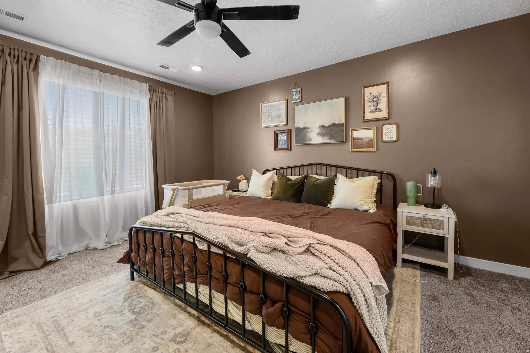 Spacious bedroom featuring neutral brown walls, a large window with blinds and drapes, recessed lighting, and a ceiling fan