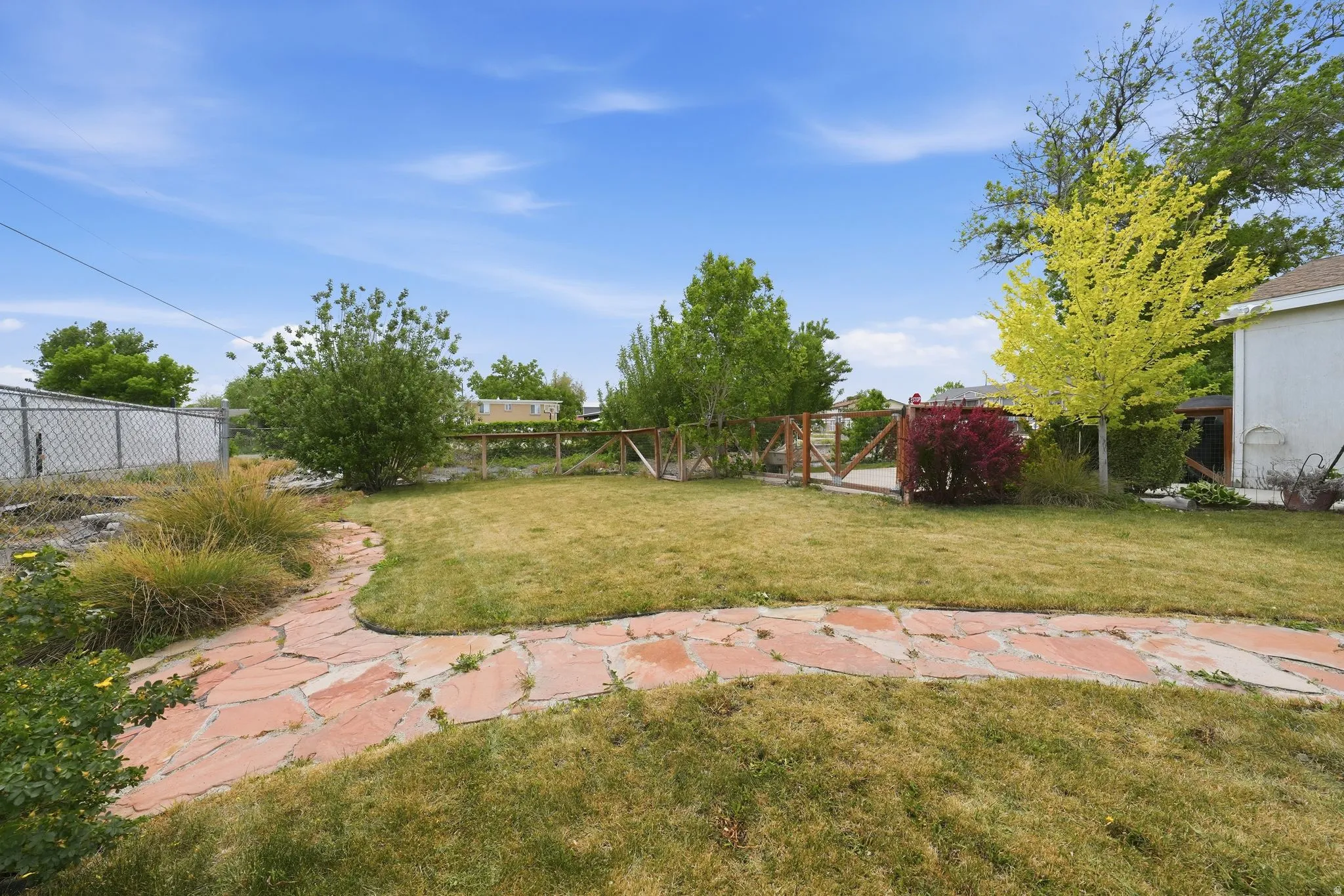 Expansive backyard featuring a winding flagstone pathway, mature trees, and shrubs providing natural screening, with a partial chain-link fence and a partial wooden fence